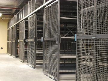 A wire partition cage with metal shelves inside, both gray in color.