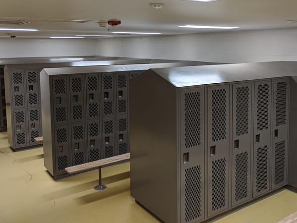 Single-tier and two-tier Heavy Duty Ventilated Athletic Lockers in a locker room, with a dark gray finish.