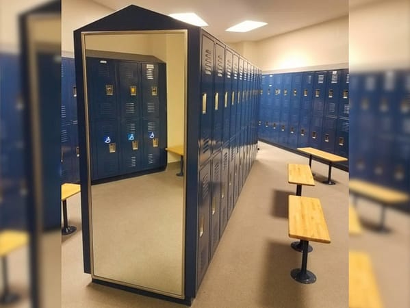 Two-tier standard lockers in a locker room in a blue finish, with a benches and a mirror as an endcap.