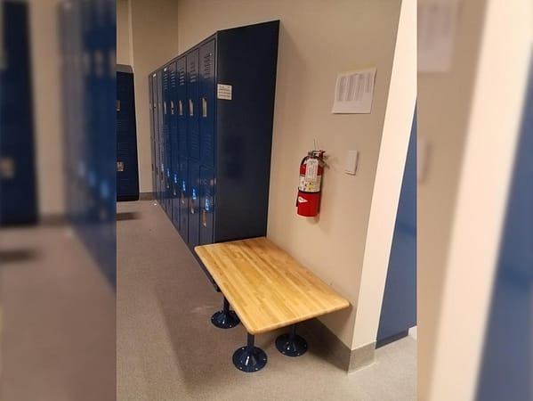 Two-tier standard lockers in a locker room in a blue finish, with a bench to aid disabled people on the side.