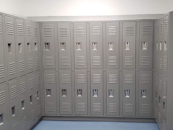 Two-tier standard metal lockers in a locker room, with a gray finish.