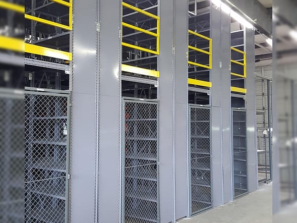 A mezzanine with yellow guard rails set up on gray metal shelving units, and wire partitioning separating the shelving at ground level.