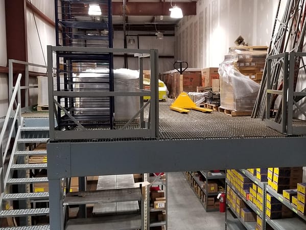 Looking towards a mezzanine that has product and a pallet jack on top with products with shelving and products below.