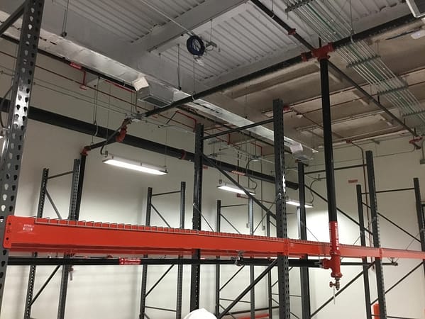 Pallet rack integrated with fire sprinklers, with black uprights, orange beams, and wire decking.