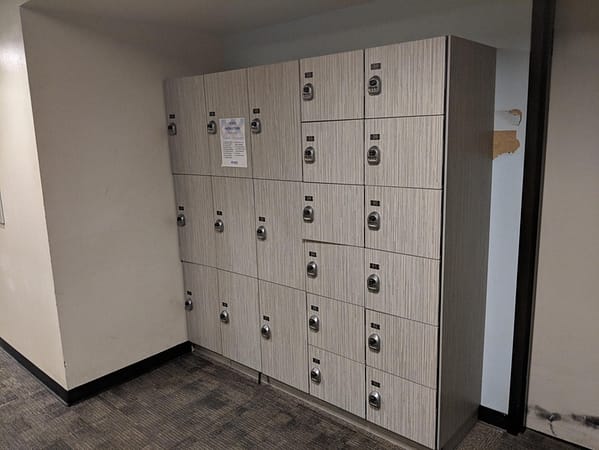 Three-tier and six-tier phenolic lockers in a hallway, with a wood style finish.