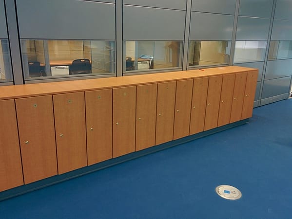 Single-tier half-height plastic laminate lockers in a hallway, with a wood finish.