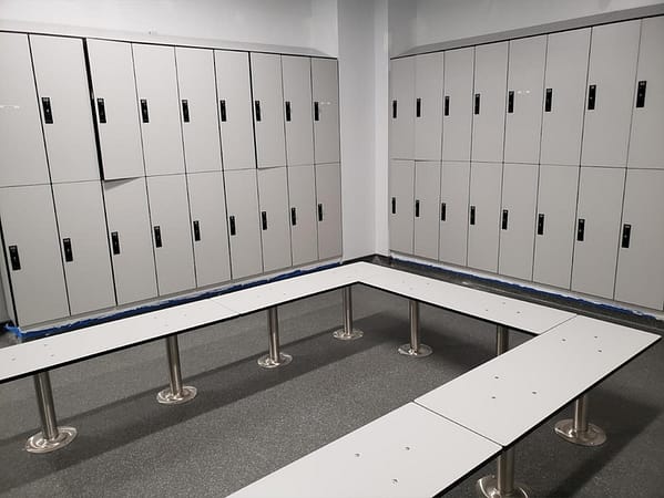 Two-tier plastic laminate lockers and benches in a locker room, with a light gray finish.