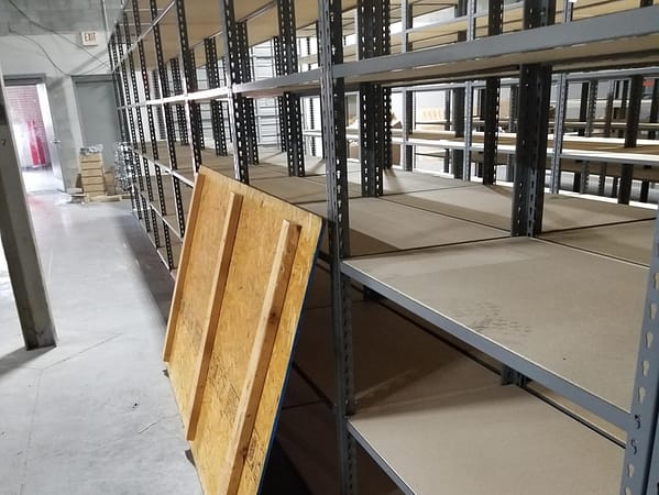 Empty rivet shelving with particle board shelving, with a gray finish in a small warehouse.