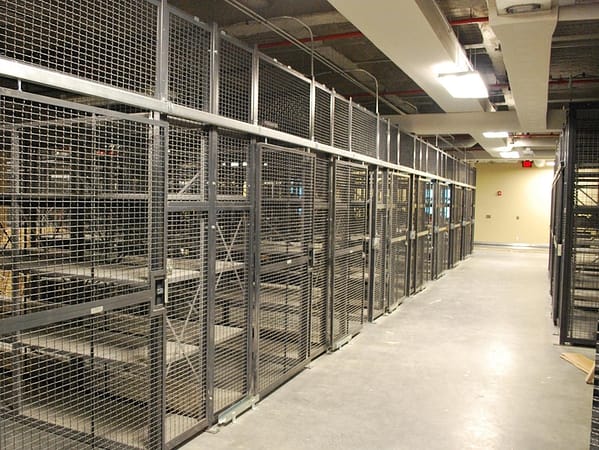 A wire partition cage with metal shelves inside, both gray in color.