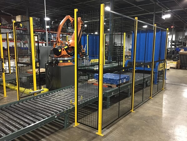 Wire partition cage functioning as a machine guarding cage containing a machine in a semi-enclosed area and a conveyor belt going through, by Wirecrafters.