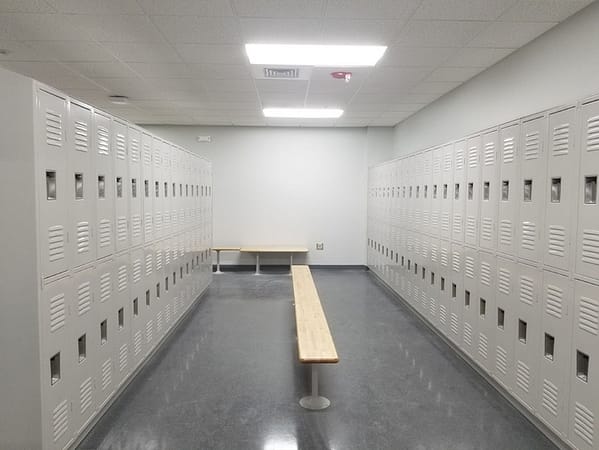 Two-tier standard lockers with an off-white finish and benches in a locker room.