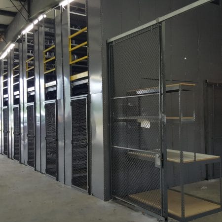 A workbench behind a wire partition, leading to gray metal shelving separated by wire partitions and using a mezzanine to increase storage.